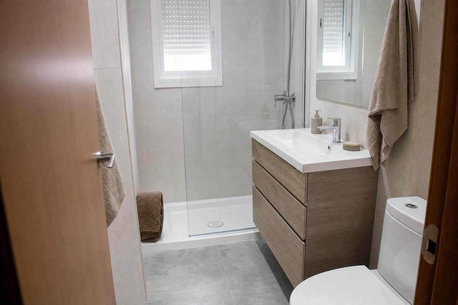 Baño pequeño reformado con plato de ducha, mampara, mueble de lavabo y azulejo claro