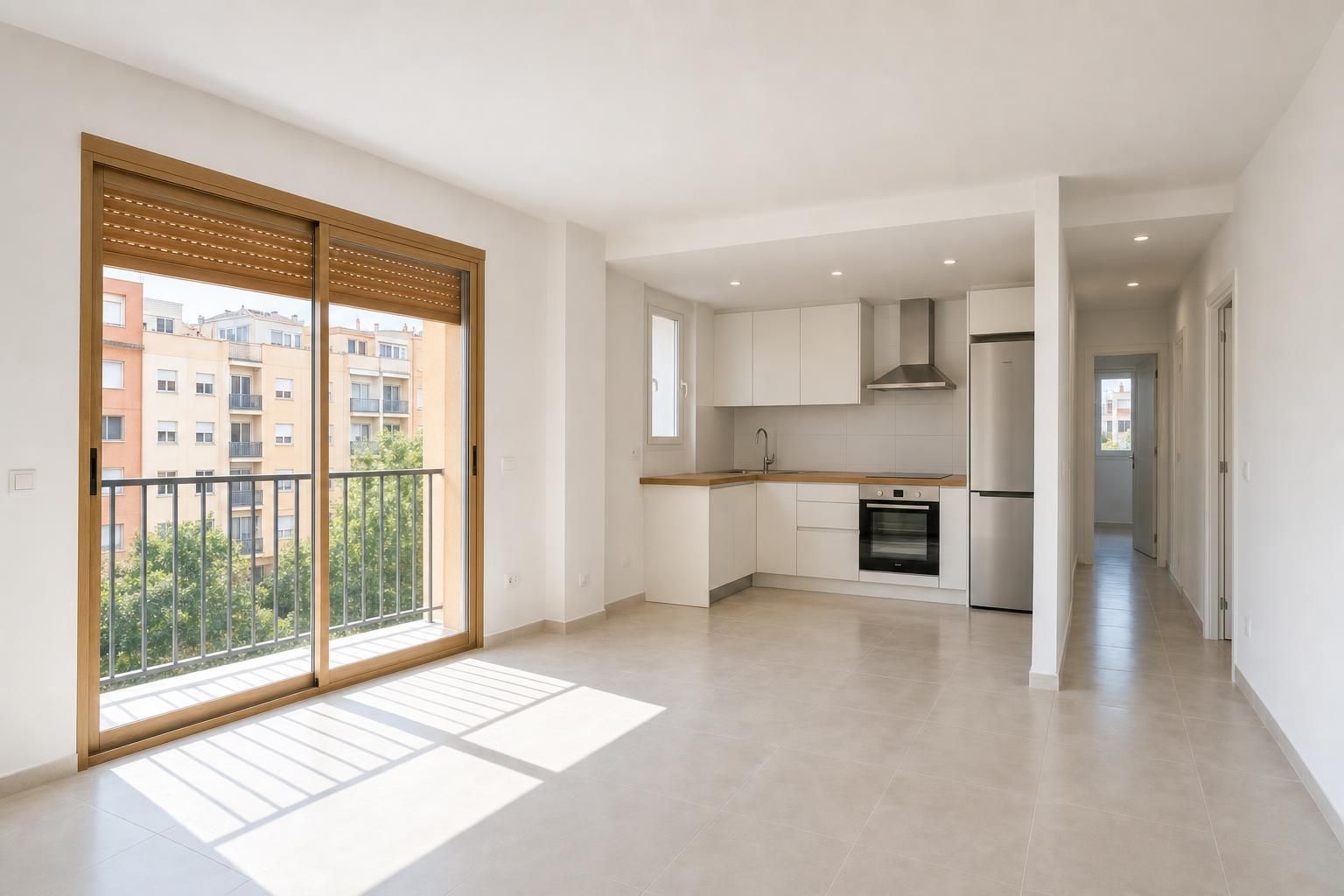 Salón de un piso reformado con suelo claro, persiana de madera sobre la puerta del balcón y la cocina al fondo
